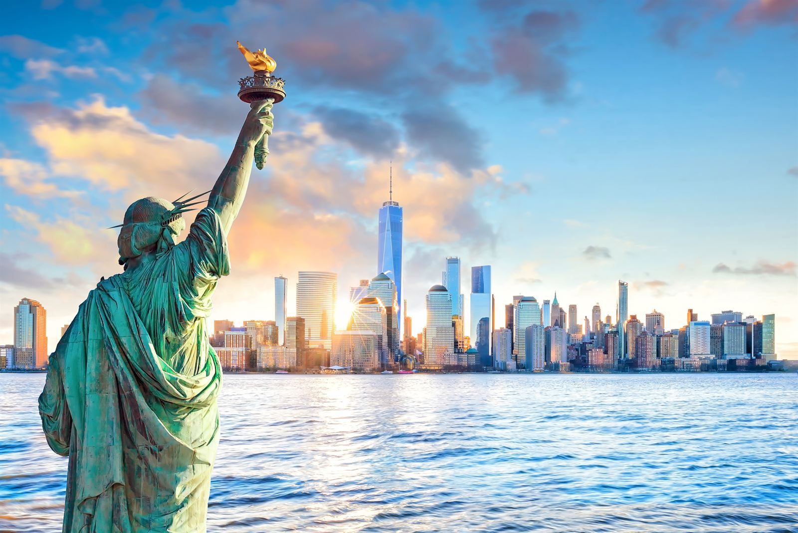 The Statue of Liberty raising her torch, with the Lower Manhattan skyline and One World Trade Center behind