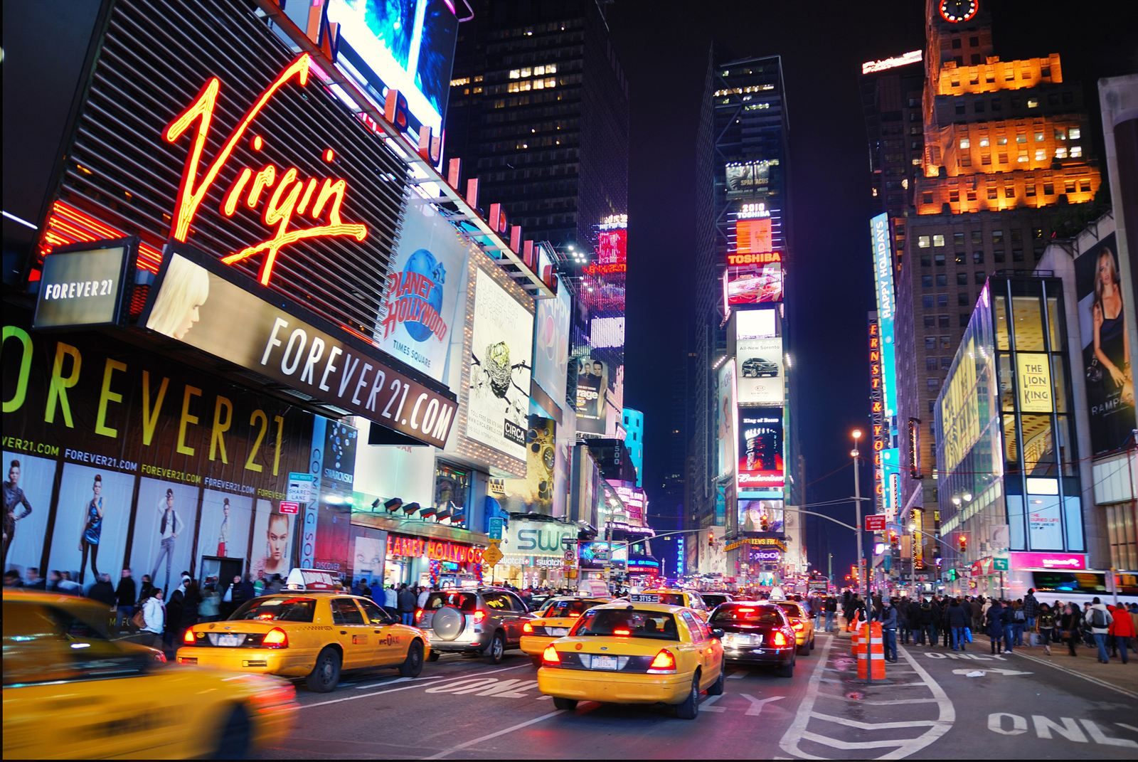 Times Square at night, with yellow taxis on Broadway beneath neon signs and video billboards